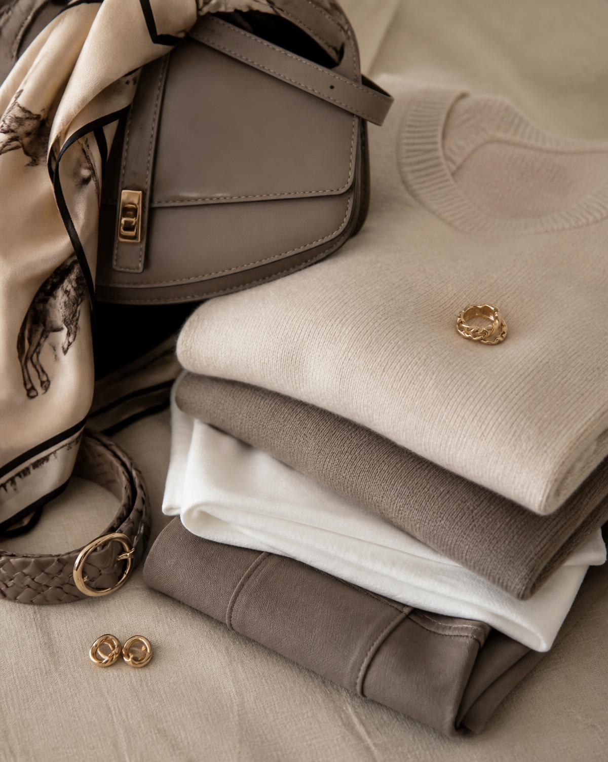 Peças neutras dobradas com acessórios em tons taupe — imagem conceitual